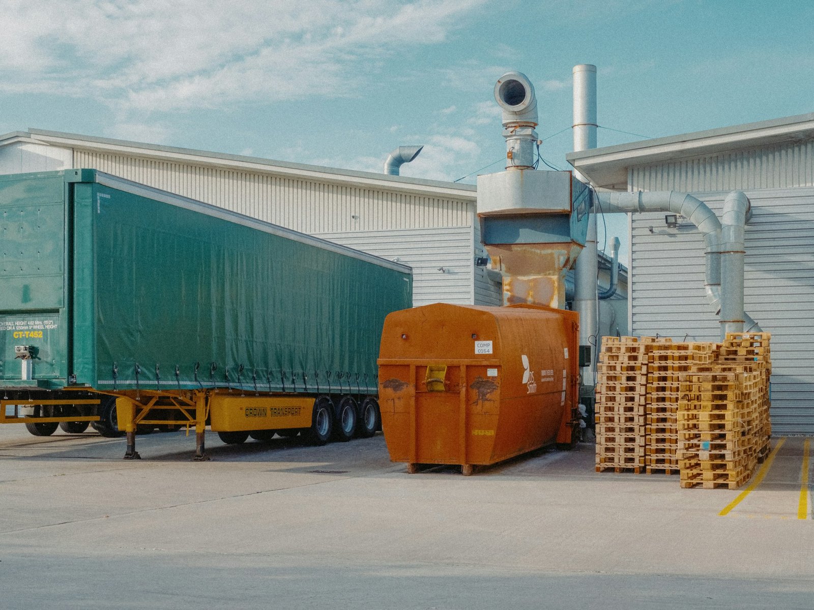 A freight trailer and pallet staging area beside a working warehouse
